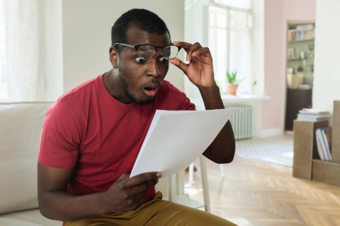 HOW much? Man looking shocked at his bills on the kitchen table