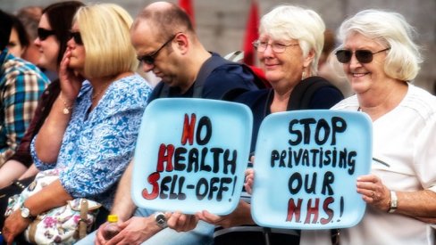 A group of protesters with signs reading "No health sell off" and "stop privatising our NHS"