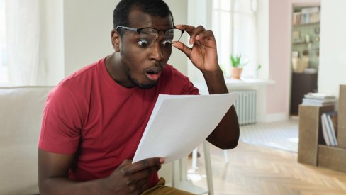 Man looking shocked at his bills on the kitchen table